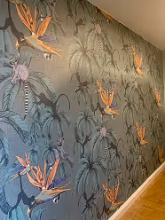 Wand mit Tapete, die einen tropischen Blumendruck mit orangefarbenen Strelitzienblüten und grünen Palmenblättern zeigt.