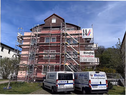 Rotes Gebäude mit Gerüst im Aufbau und zwei weißen Firmenfahrzeugen von Wohütt Maler und Bodenleger davor an einem sonnigen Tag.