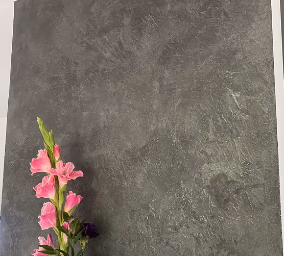 Ein Ast mit pinken Gladiolenblüten vor einem dunkelgrauen, strukturierten Hintergrund.