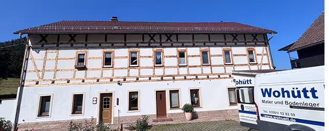 Fachwerkhaus mit Ziegeldach, davor zwei weiße Firmenfahrzeuge von Wohütt.